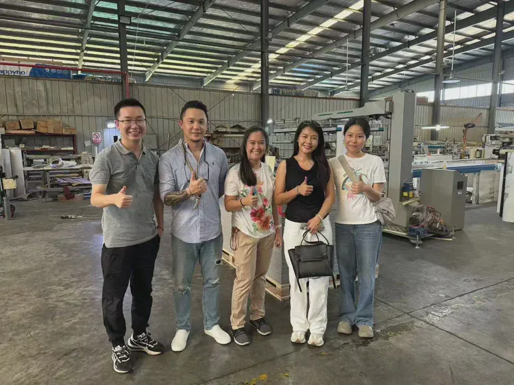 工厂参观：一组访客在厂房前合影，背景为生产车间与设备